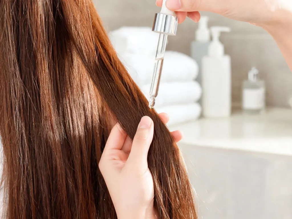 Lśniące, zdrowe, długie włosy brunetki, na które nakładane jest odżywcze serum proteinowe w minimalistycznej łazience.