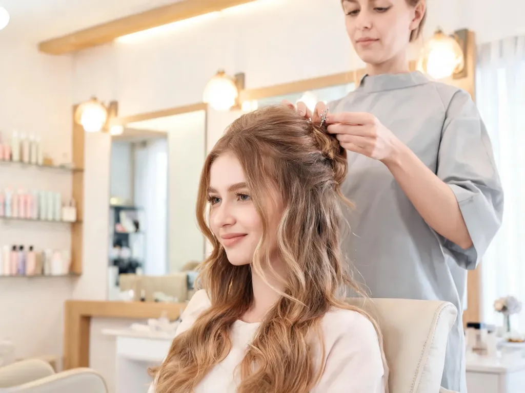 Fryzjerka upina miękkie fale młodej kobiety w elegancki kok, tworząc modną fryzurę na wesele w nowoczesnym salonie.
